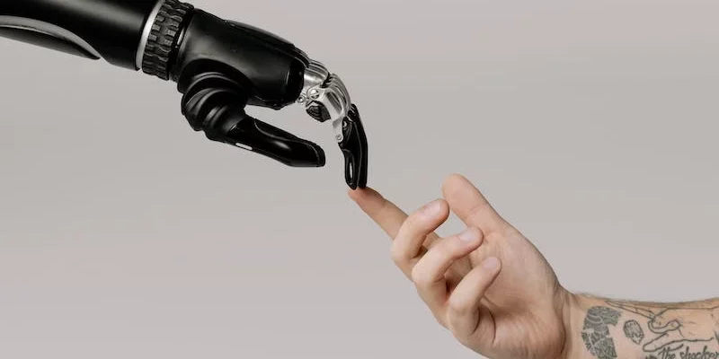 Eine männliche, tatoovierte Hand, die mit den Fingern eine robotter Hand berührt