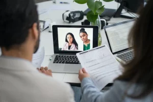 Zwei Personen schauen auf einen Laptop mit zwei Studenten im Bildschirm