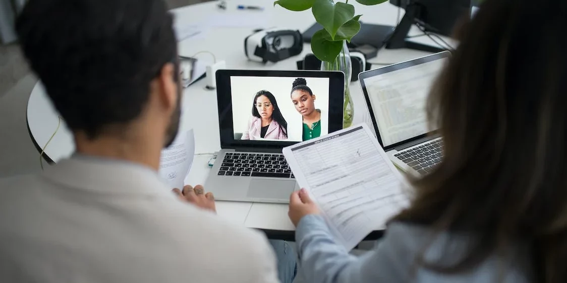 Zwei Personen schauen auf einen Laptop mit zwei Studenten im Bildschirm