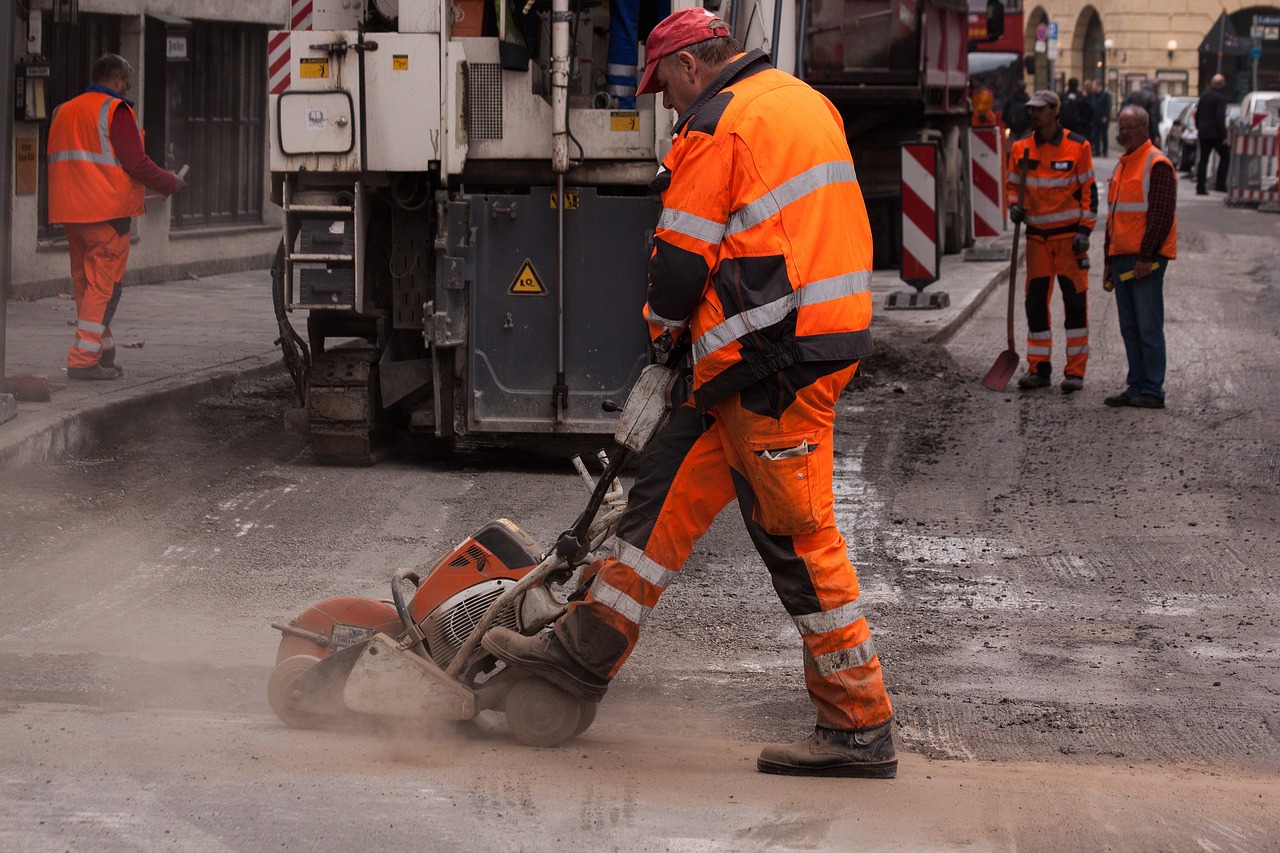 Bauarbeiter in orangener Arbeitskleidung teert eine Straße