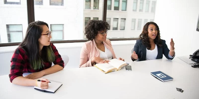 Drei Frauen, sitzen an einem Tisch und führen eine Diskussion