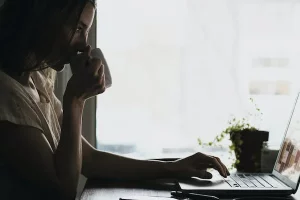 Frau sitzt in einem dunklen Raum mit einem Kaffe an ihrem Laptop