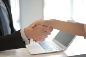 Ein Mann in einem Anzug schüttelt einer Frau in einer weißen Bluse die Hand