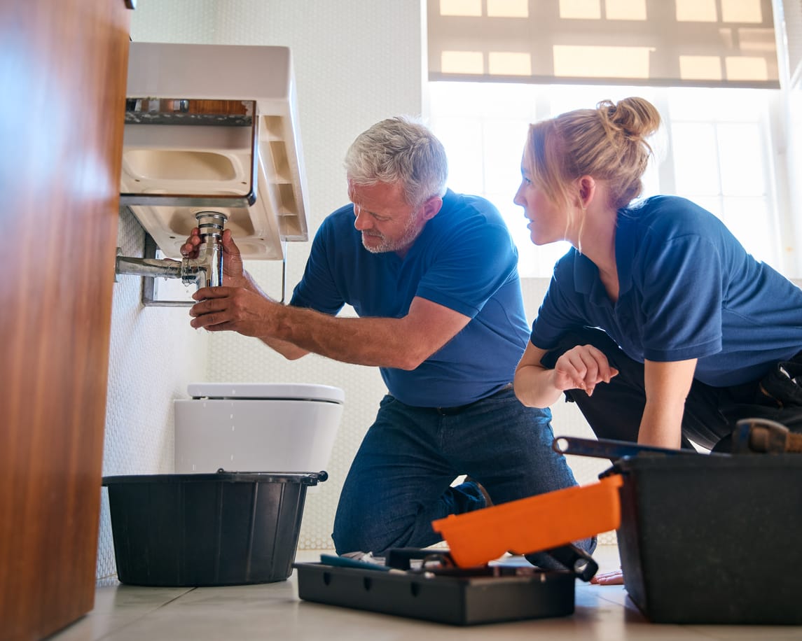 Ausbilder zeigt Auszubildender die Reparatur eines Waschbeckens